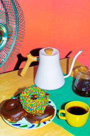Photo of a gooseneck kettle, a plate of doughnuts, a mug of coffee and a carafe.